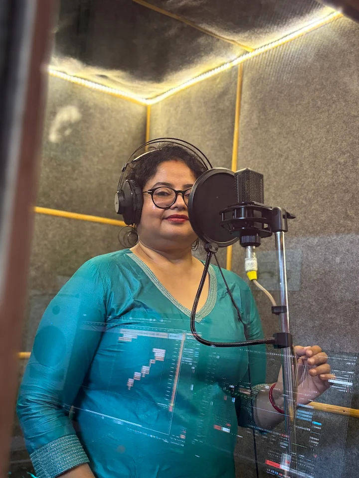 Singer at a condenser microphone in the vocal booth, with the recording session reflected on the glass